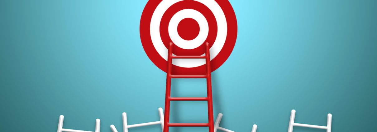 Eine rote Leiter reicht bis zu einer großen rot-weißen Zielscheibe auf blaugrünem Hintergrund und erinnert so an das Setzen neuer Ziele beim Jahreswechsel, während an ihrem Fuß mehrere andere weiße Leitern verstreut liegen.