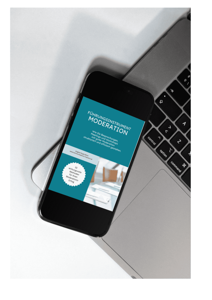Ein Smartphone mit der Webseite „Führungsinstrument Moderation“ liegt auf der Tastatur eines Laptops. Die Seite enthält Text und eine kreisförmige Grafik. Die Umgebung scheint ein Arbeitsplatz zu sein, unter dem Laptop ist ein Teil eines Schreibtischs sichtbar.