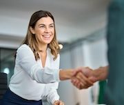 Eine Frau in Geschäftskleidung lächelt und schüttelt einer anderen Person in einer Büroumgebung die Hand. Sie wirkt freundlich und professionell - ganz im Sinne des Seminars Abenteuer Kommunikation.